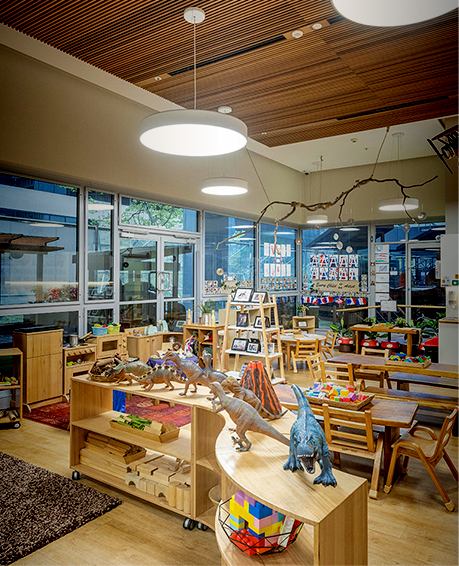 Column image Early childhood centre classroom with wooden furniture, dinosaur toys, and learning play areas