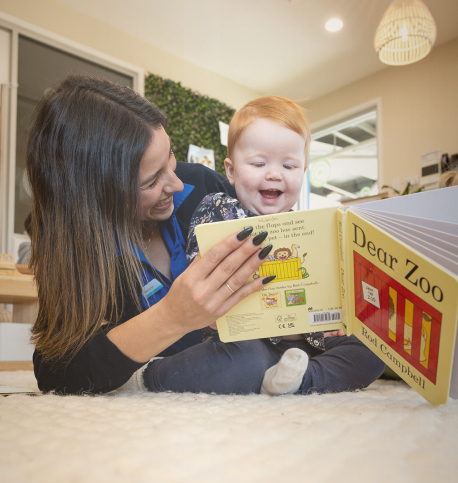 Column image Childcare educator reading a book to a baby during learning time