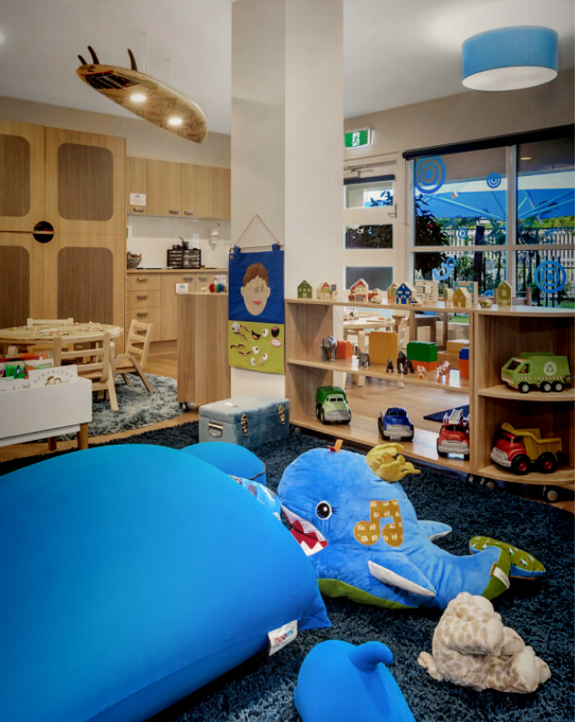 Column image Childcare ocean-themed playroom with blue soft seating, wooden furniture and toy vehicles