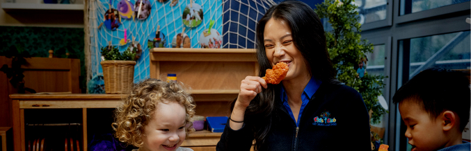 Column image Early learning educator sharing mealtime with children in classroom