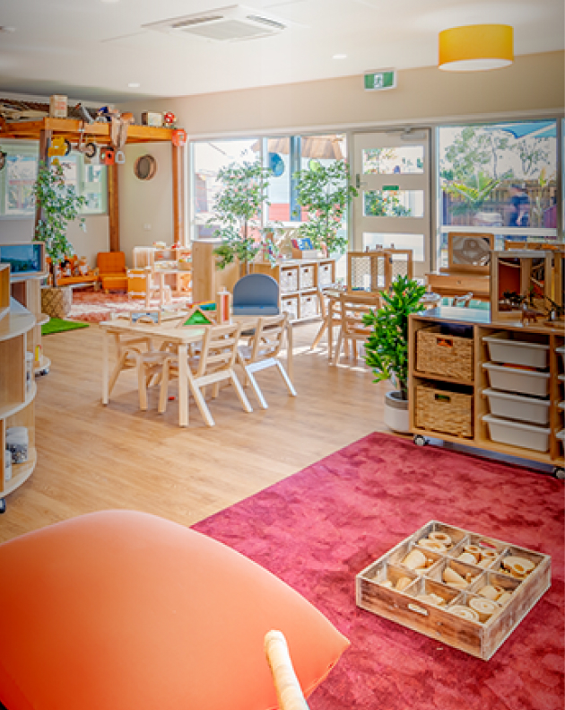 Column image Childcare classroom with wooden furniture, play-based learning setup, plants and open activity areas