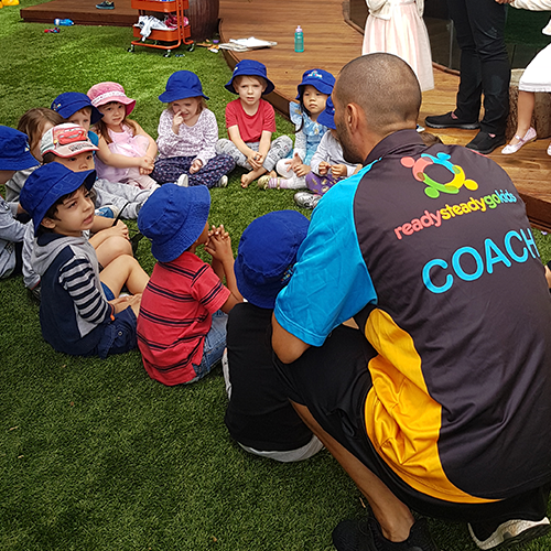 Column image Children participating in a group sports extracurricular activity with a coach at Kids Club childcare centre during active learning and teamwork play.