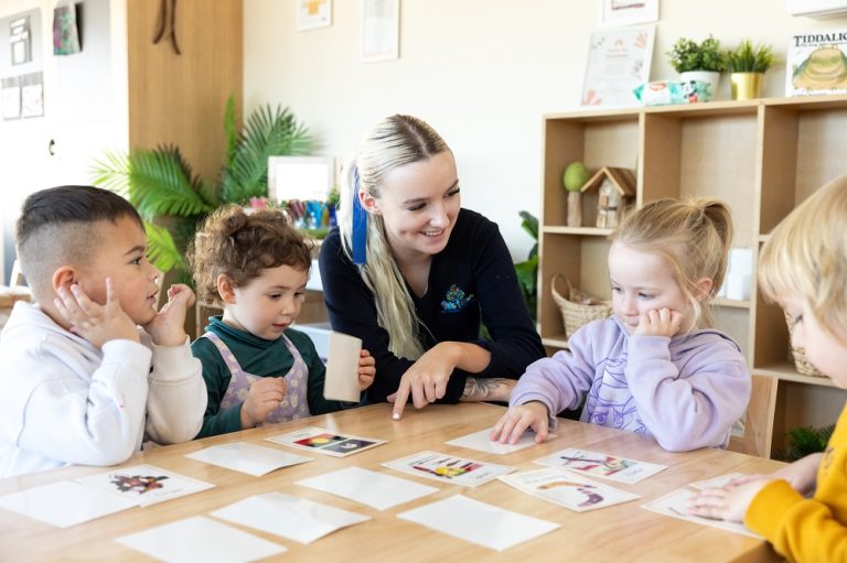 Carousel image Educator engaging children in a collaborative learning activity at Kids Club Childcare Centre within a welcoming and supportive classroom environment.