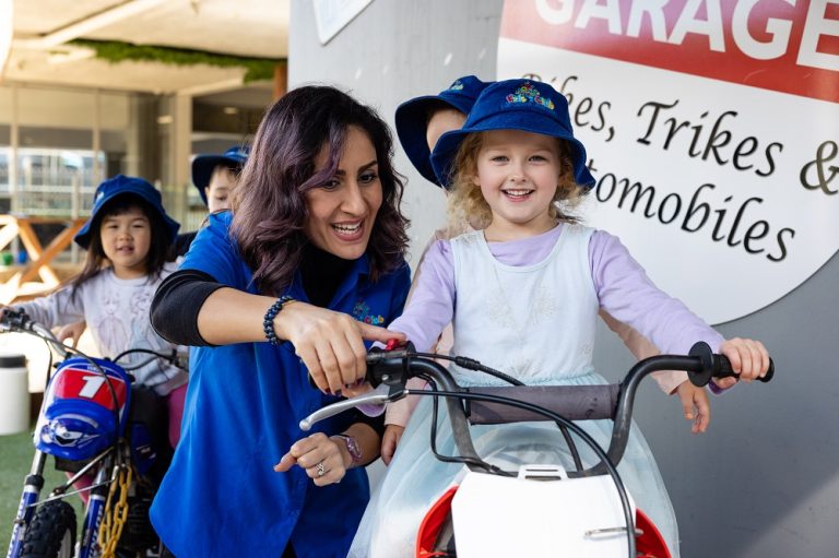 Carousel image Educator supporting children during imaginative outdoor play in a safe and engaging learning environment at Kids Club Childcare Centre.