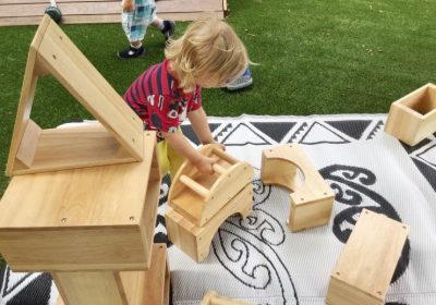 Column image Child engaged in outdoor construction play with wooden blocks at a Kids Club childcare centre