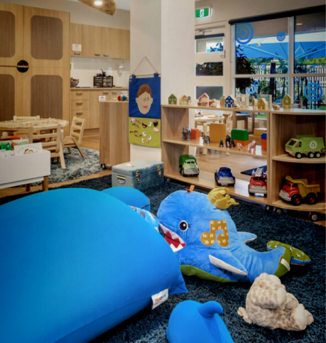 Column image Children's ocean-themed playroom at an early learning centre featuring blue soft furnishings, toy vehicles, wooden play areas and a shark cushion.